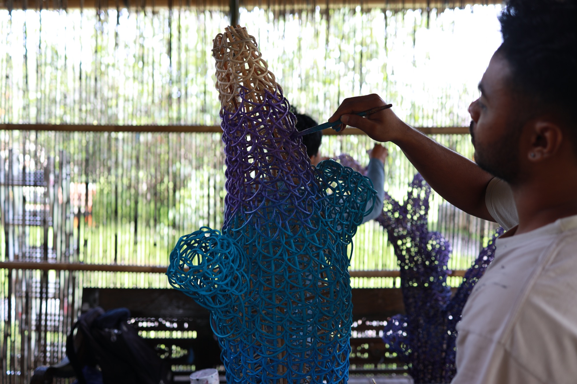 An artisan hand-painting a woven sculpture at Art Village